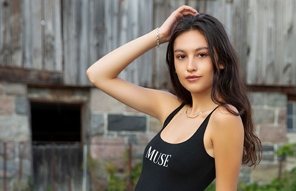 Beautiful young woman wearing a black bodysuit with the word Muse on the front